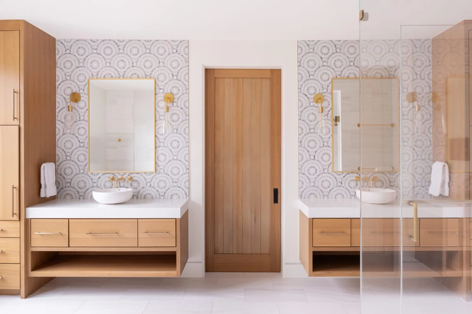 A double vanity in a bath with patterned wall tile and a walk-through shower