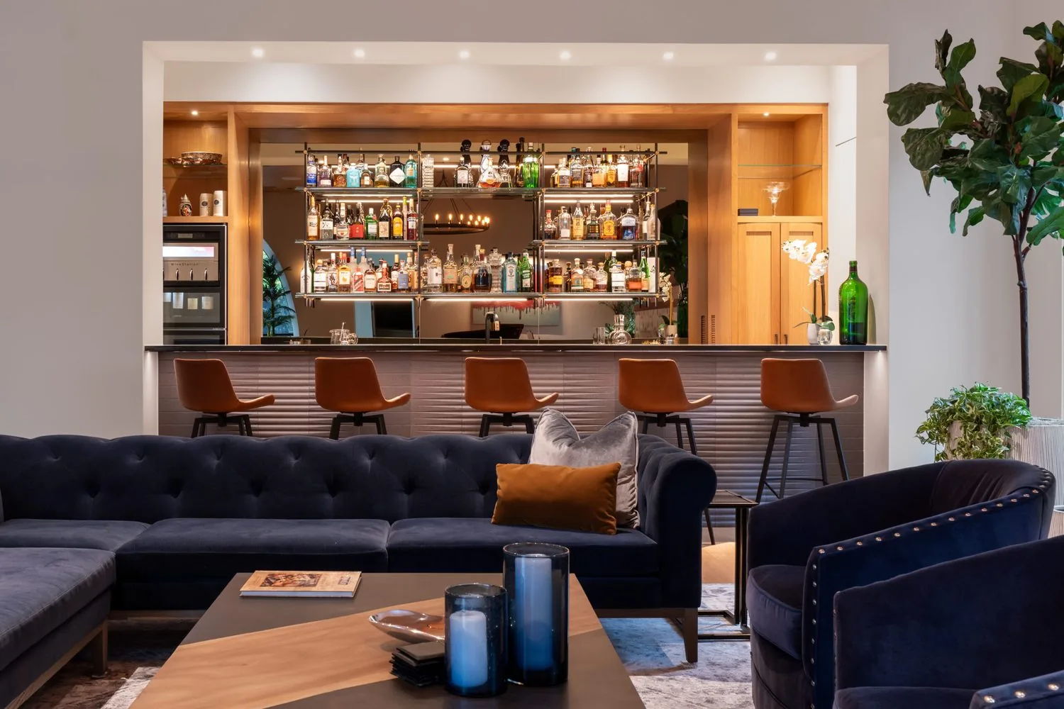 A backlit home bar with leather stools and a navy sectional