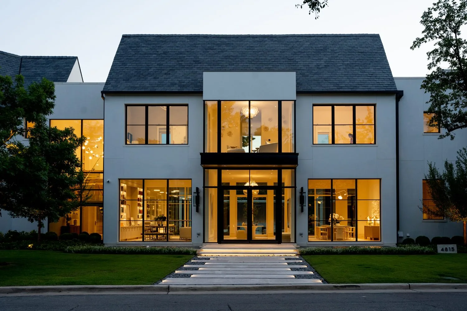 A slate-roofed front elevation lit from inside at dusk
