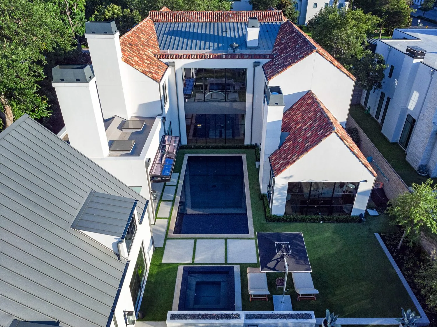 An aerial view of a tile-roofed house wrapped around a long pool courtyard