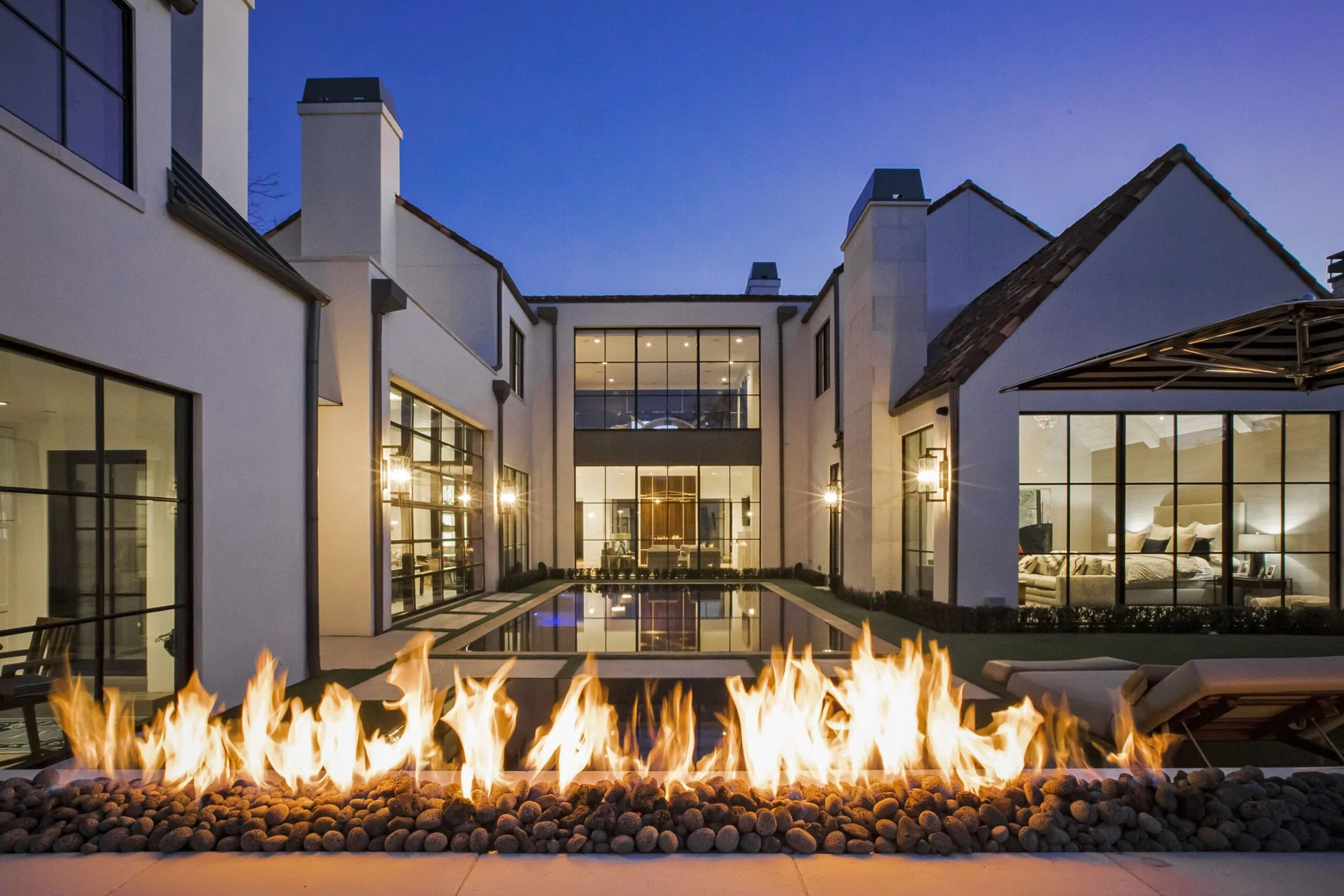 A Platinum Series Homes courtyard at dusk, with a linear fire feature reflecting off the pool