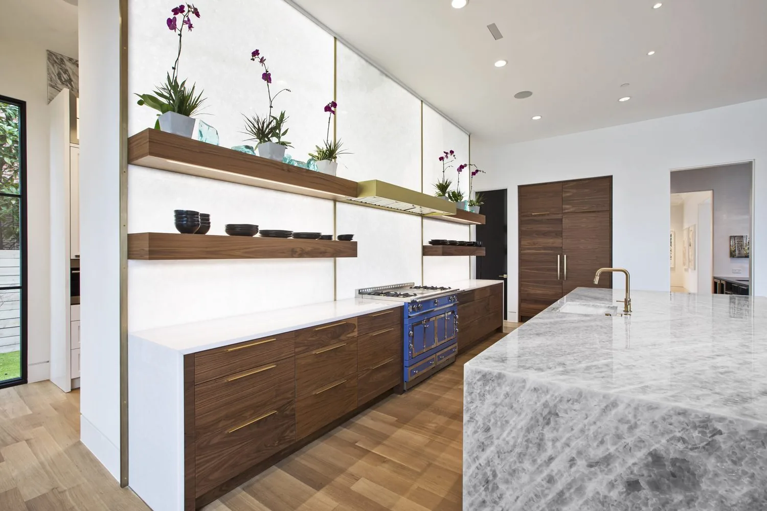 A walnut and white kitchen with floating shelves and a marble island