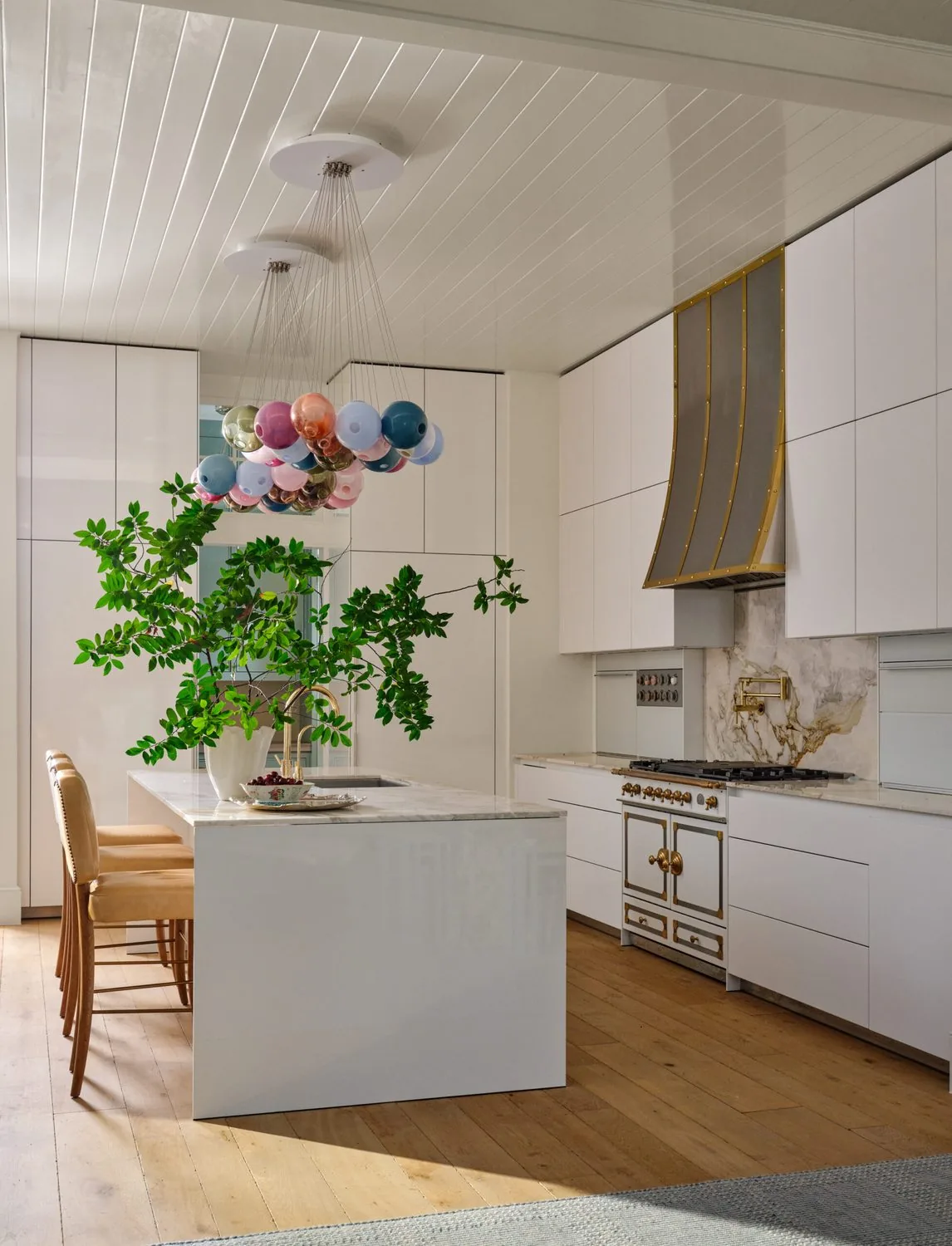 A white kitchen with a sculptural island and a range in a plaster alcove