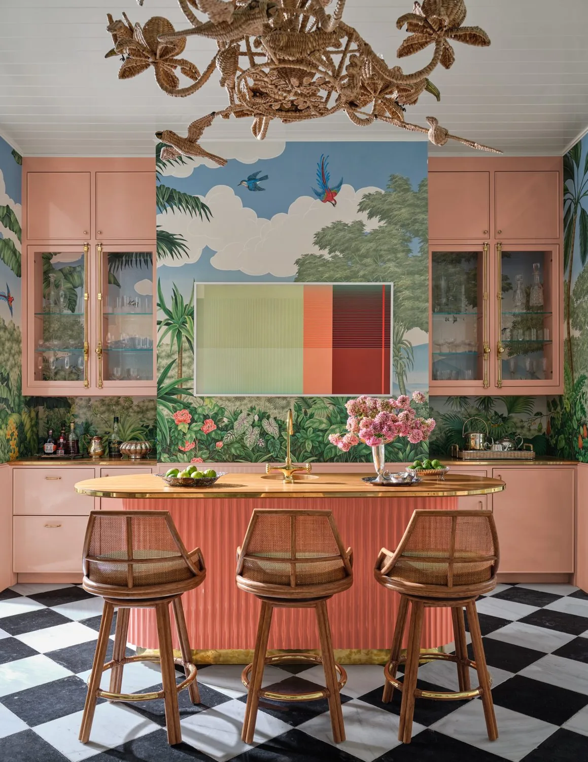 A kitchen with a checkerboard stone floor, coral cabinetry and a hand-painted mural