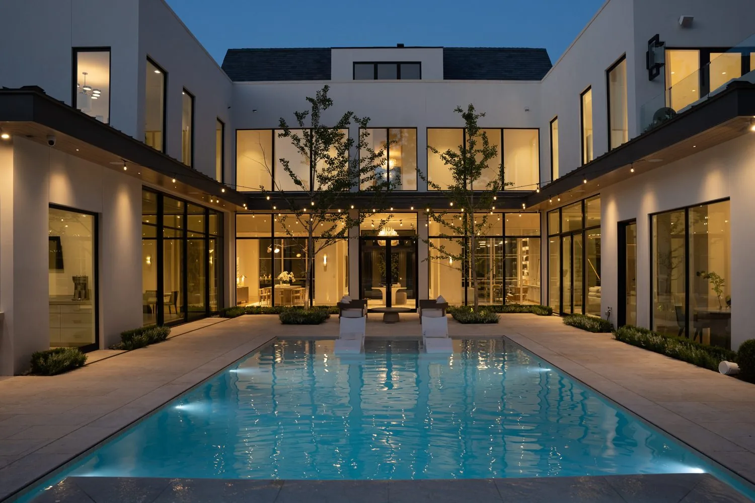 A courtyard swimming pool at dusk framed by lit glass walls